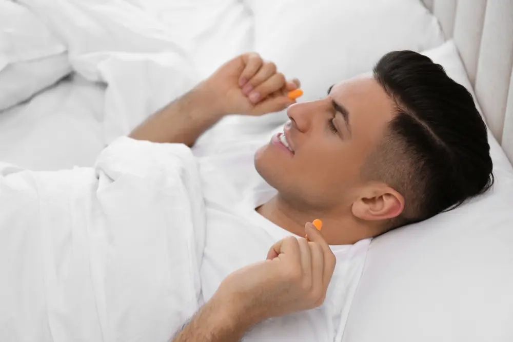 Man inserting foam earplugs in bed.