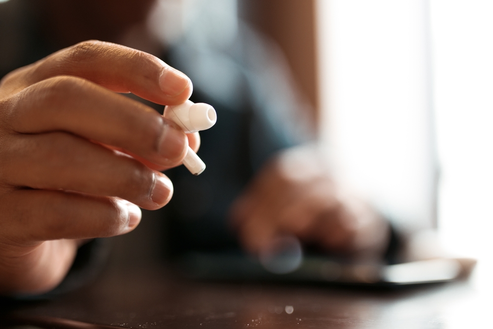 man's hand holding an AirPod sitting at a cafe table.